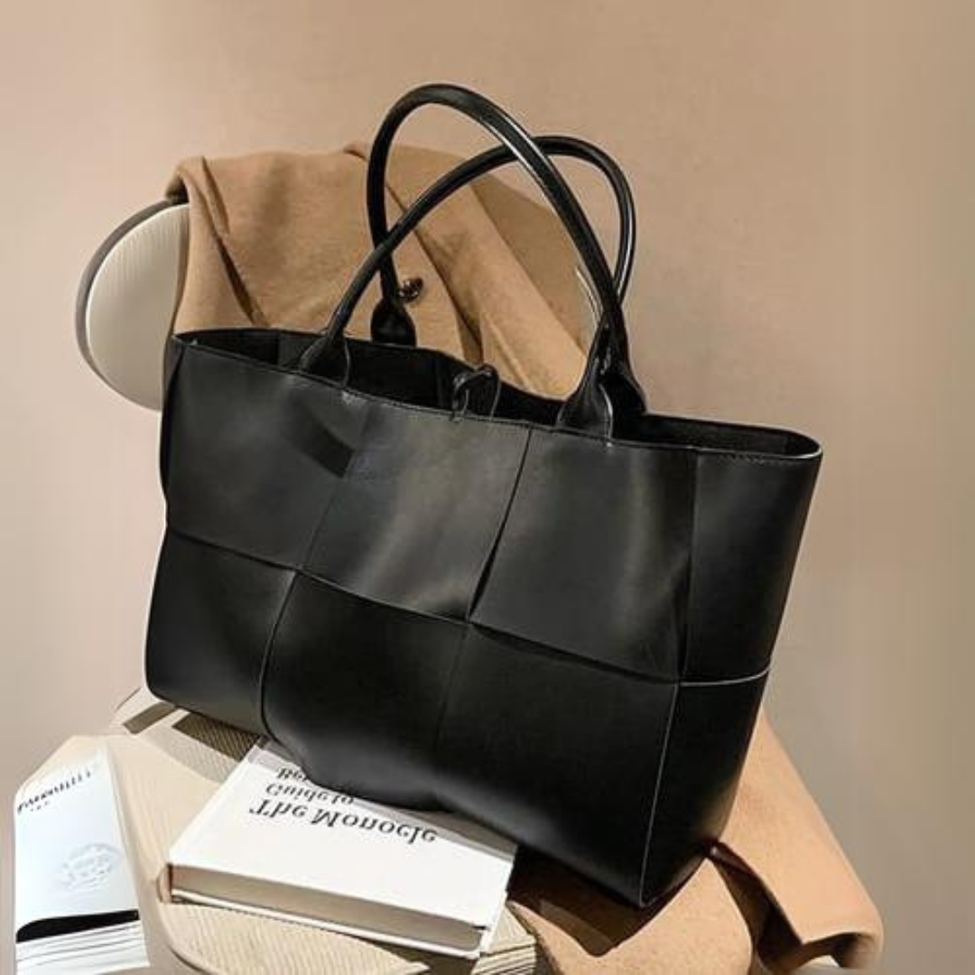 Schwarze Lederhandtasche auf beigem Mantel und Stuhl, elegantes Design, hochwertige Verarbeitung, modisches Accessoire für Damen.