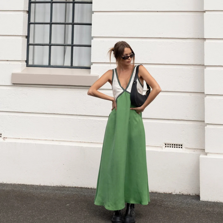 Frau in grünem Maxikleid und Sonnenbrille vor weißer Wand, trägt schwarze Tasche und Stiefel. Streetstyle, Mode, Sommeroutfit.