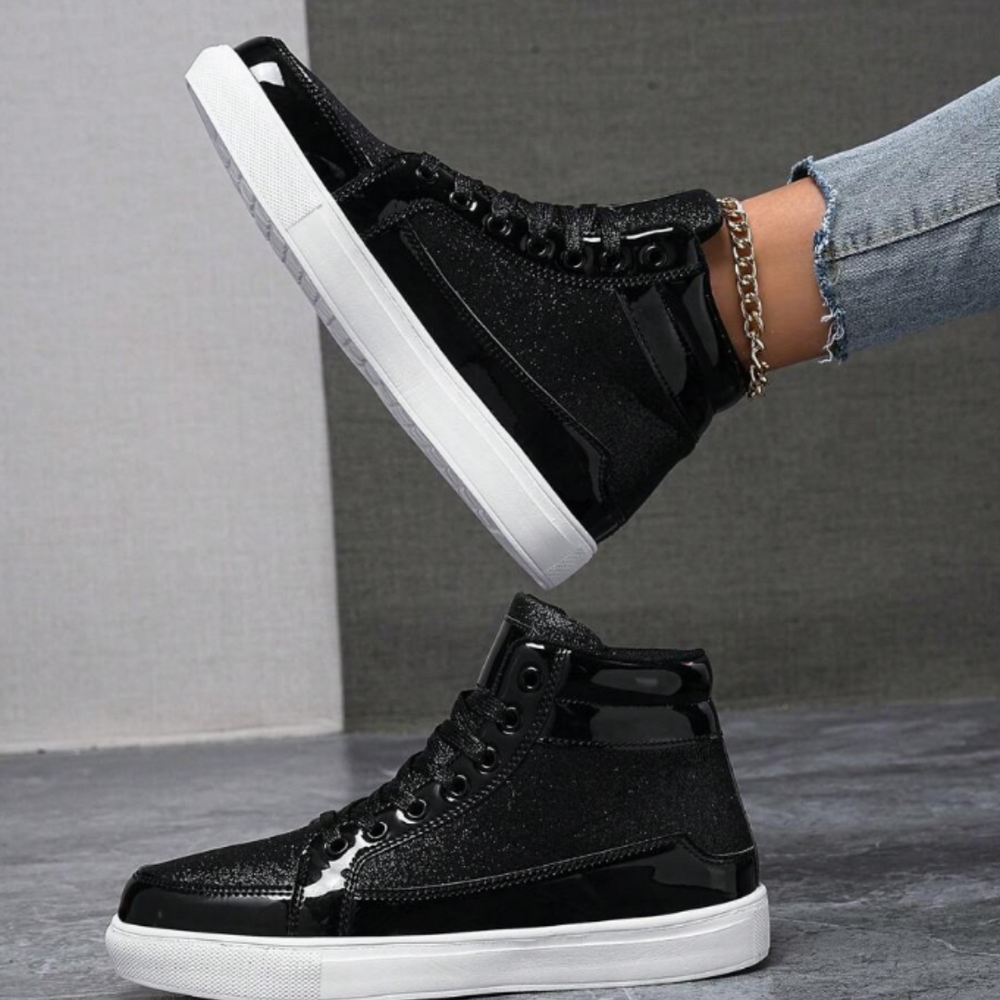 Schwarze Glitzer-Sneaker mit weißer Sohle, getragen von Person in blauer Jeans. Modische, glänzende High-Top-Schuhe, ideal für trendige Streetwear.