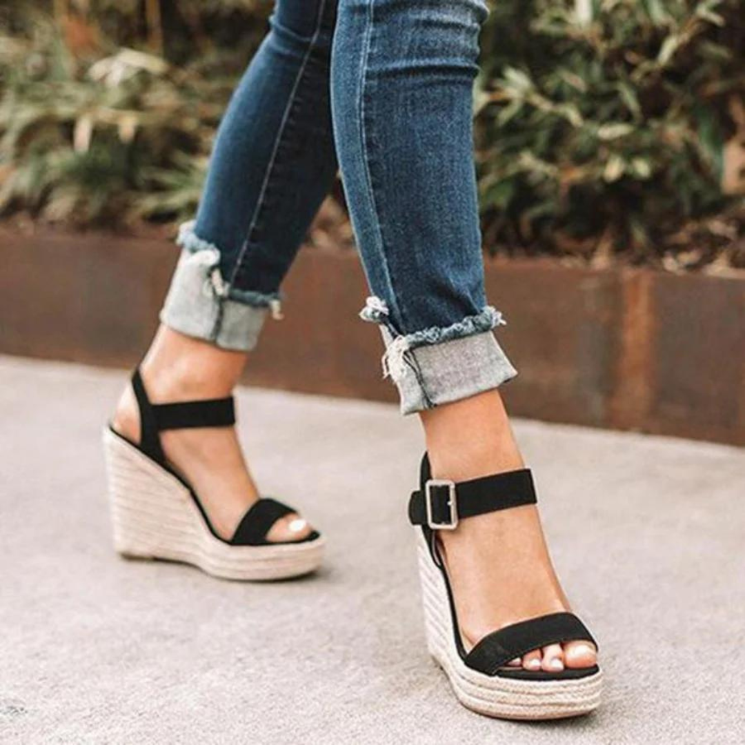 Damen Sandalen mit Keilabsatz, schwarzem Riemen und Schnalle, kombiniert mit hochgekrempelten Jeans. Sommermode, bequeme Schuhe, trendiger Look.
