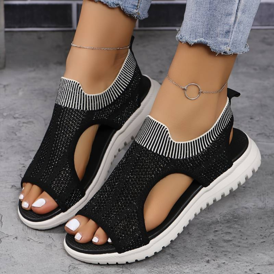 Schwarze Damen-Sandalen mit weißer Sohle, gestricktem Obermaterial und silbernem Knöchelarmband, getragen mit hellblauen Jeans.