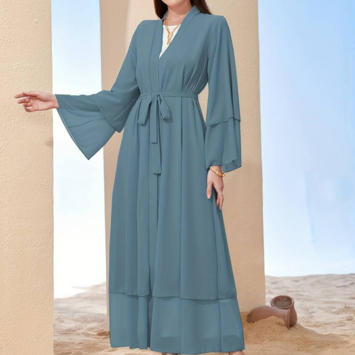 Frau in langem, blauem Kimono-Kleid mit Gürtel, stehend vor beigem Hintergrund. Elegante Mode, lässiger Stil, Sommerkleidung.