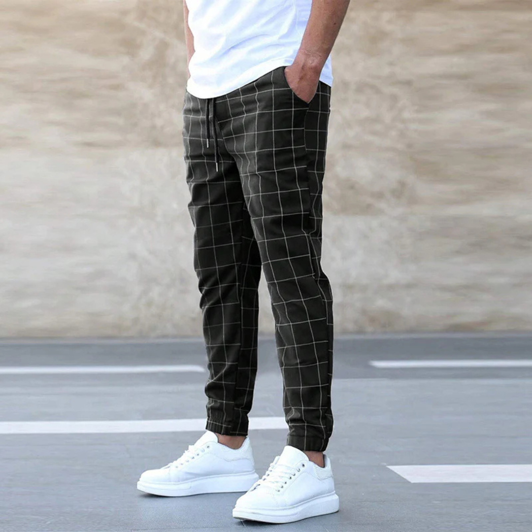 Mann in karierten Jogginghosen und weißen Sneakers vor neutralem Hintergrund. Bequeme Freizeitmode, Herrenbekleidung, stilvolle Jogginghose.