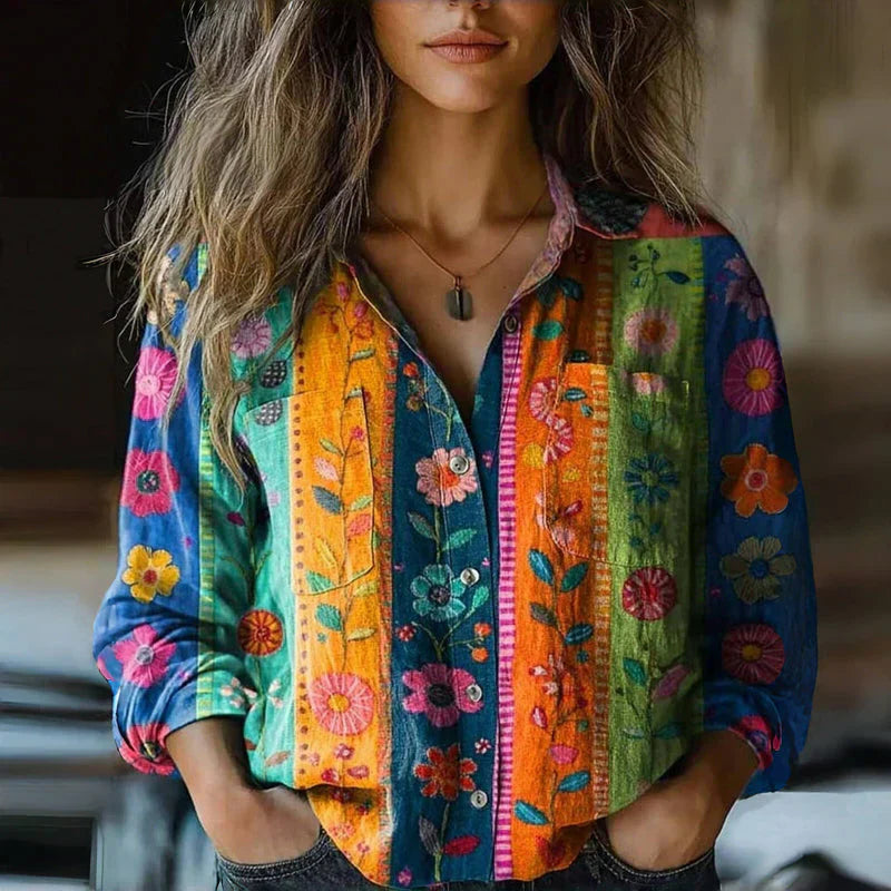 Frau trägt bunte, florale Bluse mit gestickten Blumenmustern, lässiger Stil, modisches Design, Herbstmode, lebendige Farben, Freizeitkleidung.