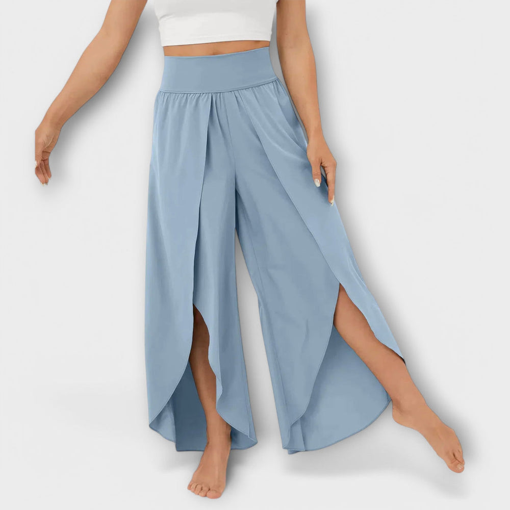 Frau trägt weite, hellblaue Hosen mit hohem Bund und seitlichen Schlitzen, kombiniert mit einem weißen Crop-Top. Modetrend, Damenbekleidung, Sommerlook.