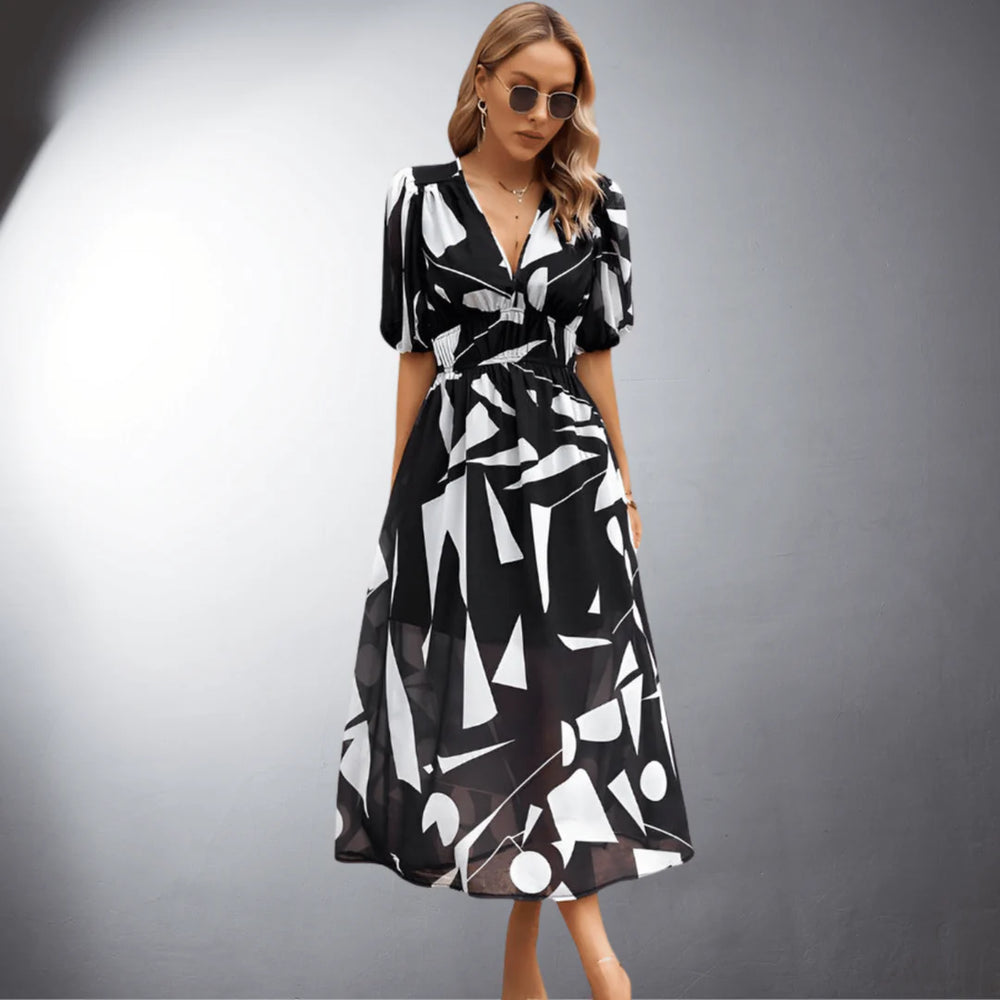 Frau in schwarz-weißem geometrischem Kleid, Sonnenbrille, vor grauem Hintergrund. Modetrend, Sommerkleid, stilvolle Damenmode.
