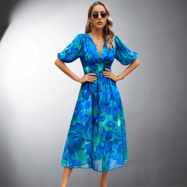 Blaues Sommerkleid mit Blumenmuster, V-Ausschnitt und Puffärmeln, getragen von Frau mit Sonnenbrille. Elegantes Damenmode-Outfit für warme Tage.