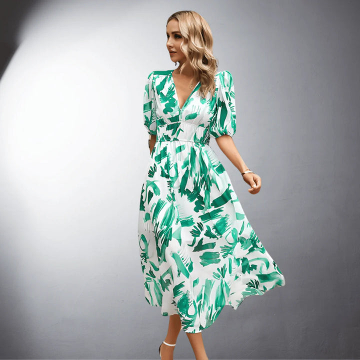 Frau in grün-weißem Sommerkleid mit Blattmuster, stehend vor grauem Hintergrund. Elegantes Design, modische Damenbekleidung, Freizeitkleid.