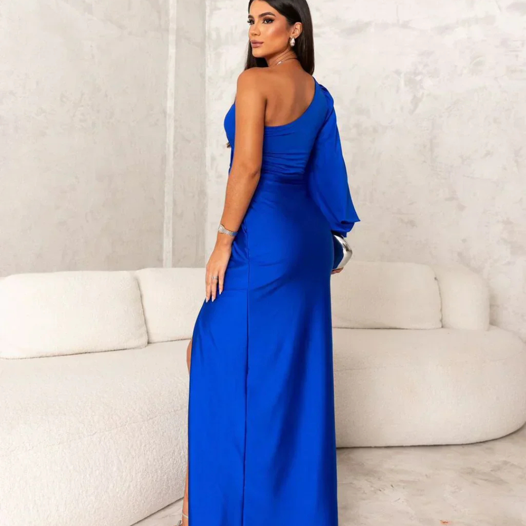 Frau in elegantem, blauem, schulterfreiem Abendkleid posiert vor weißem Sofa. Mode, Abendgarderobe, Damenbekleidung, stilvoll, modern.