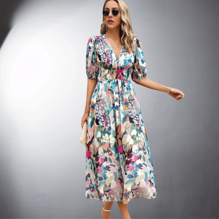 Frau in geblümtem Maxikleid, Sonnenbrille und Sandalen vor grauem Hintergrund. Sommermode, elegantes Design, florales Muster.