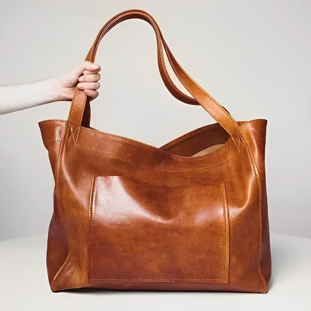 Hand hält große braune Ledertasche mit breiten Trägern und Fronttasche. Stilvolle, geräumige Damenhandtasche aus hochwertigem Leder.