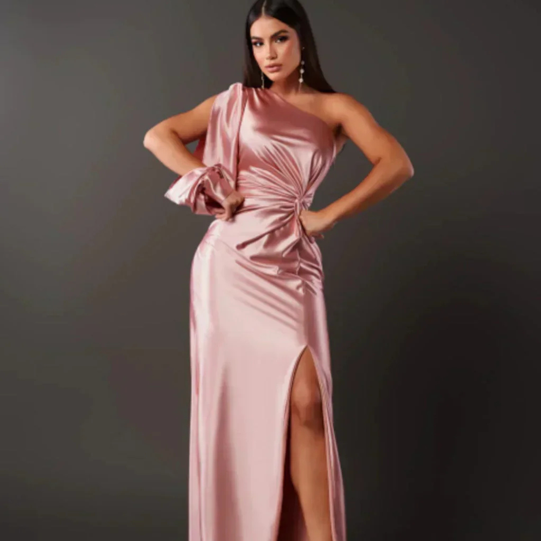 Eine Frau in einem eleganten, rosafarbenen, schulterfreien Abendkleid mit hohem Beinschlitz, posiert vor einem dunklen Hintergrund.