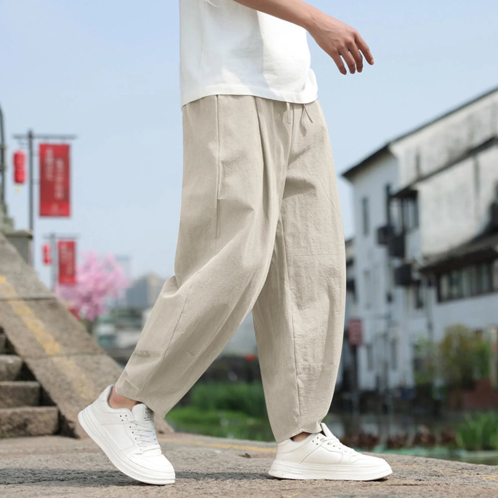 Mann in beigen Leinenhosen und weißen Sneakers auf einer Treppe, moderne Mode, urbaner Hintergrund, lässiger Stil, Frühlingsoutfit.