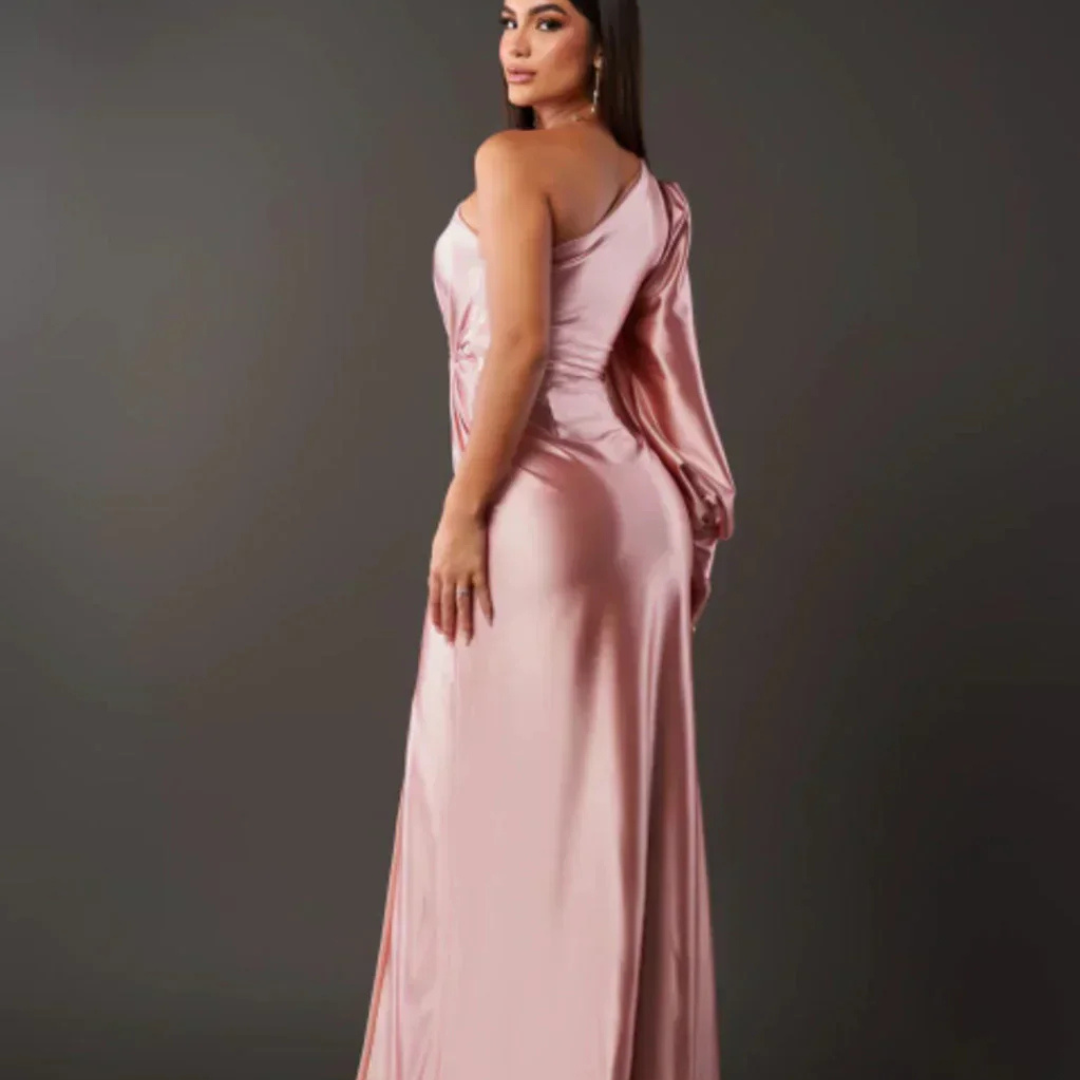 Eine Frau in einem eleganten, rosa Abendkleid mit asymmetrischem Schnitt posiert vor einem dunklen Hintergrund. Mode, Abendkleid, Damenmode.