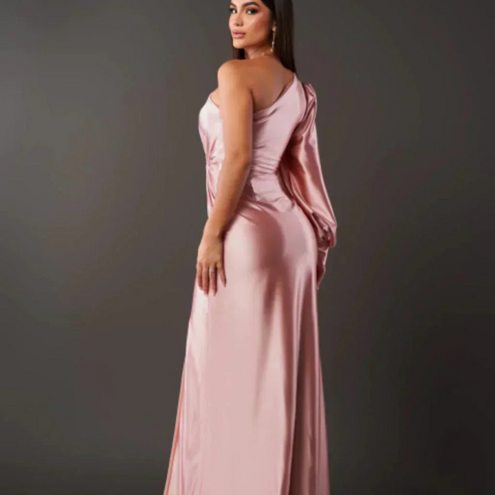 Eine Frau in einem eleganten, rosa Abendkleid mit asymmetrischem Schnitt posiert vor einem dunklen Hintergrund. Mode, Abendkleid, Damenmode.