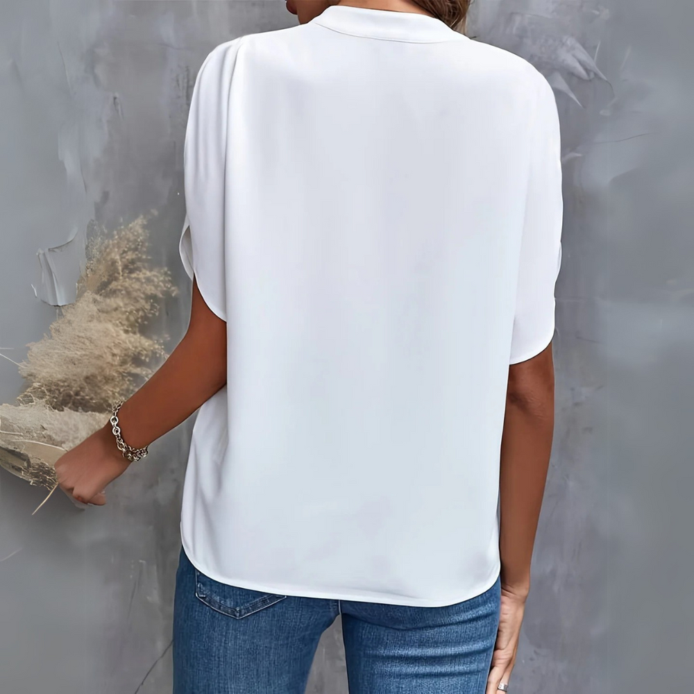 Frau in weißer Bluse und blauer Jeans von hinten, hält getrocknete Blumen. Elegante Freizeitmode, minimalistischer Stil.