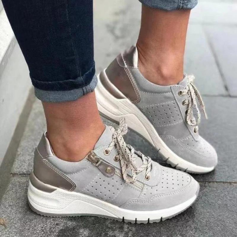 Graue Damen-Sneaker mit weißer Sohle und Schnürsenkeln, getragen auf Gehweg. Modische Freizeitschuhe, ideal für Alltag und Sport.