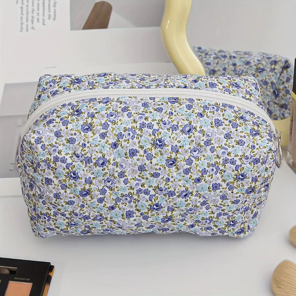 Blumige Kosmetiktasche mit Reißverschluss, blau-lila Blumenmuster, auf Schminktisch mit Spiegel und Make-up-Pinseln. Ideal für Reisen und Aufbewahrung.