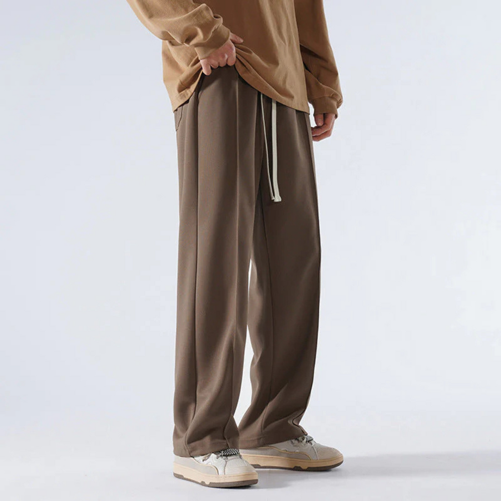 Mann in brauner Jogginghose und beigem Pullover, lässiger Stil, weiße Sneakers, Mode für Herren, bequeme Freizeitkleidung.