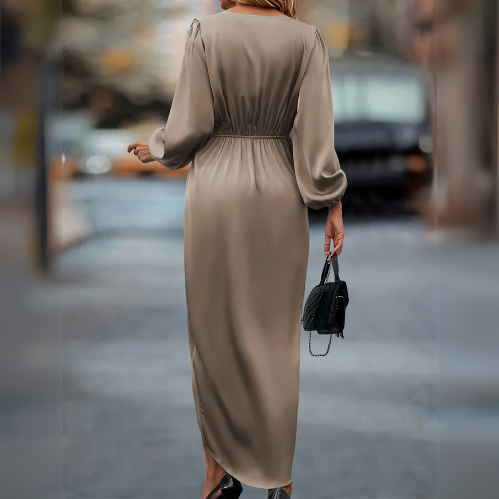 Frau in langem, beigem Kleid mit Puffärmeln, hält schwarze Handtasche, geht auf städtischer Straße. Elegante Mode, Streetstyle, Herbstoutfit.