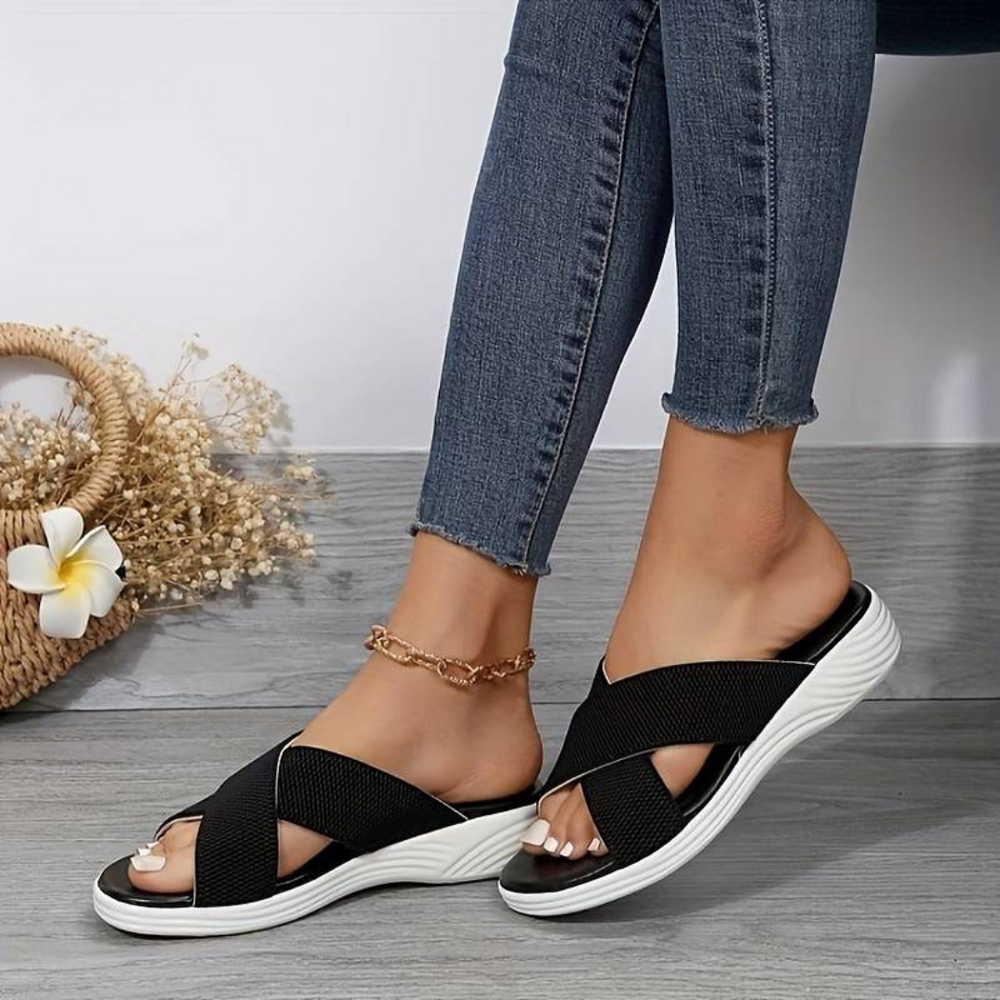 Frau trägt schwarze Sandalen mit weißer Sohle, kombiniert mit blauen Jeans. Modische Sommerschuhe, bequem und stilvoll.