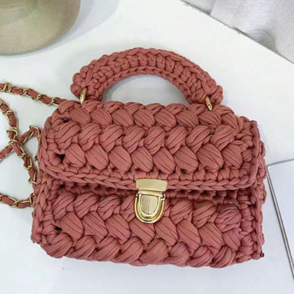 Handgefertigte rosa Häkeltasche mit goldener Kette und Verschluss, auf weißem Hintergrund. Modische Accessoires, Damenmode, Stricktasche.