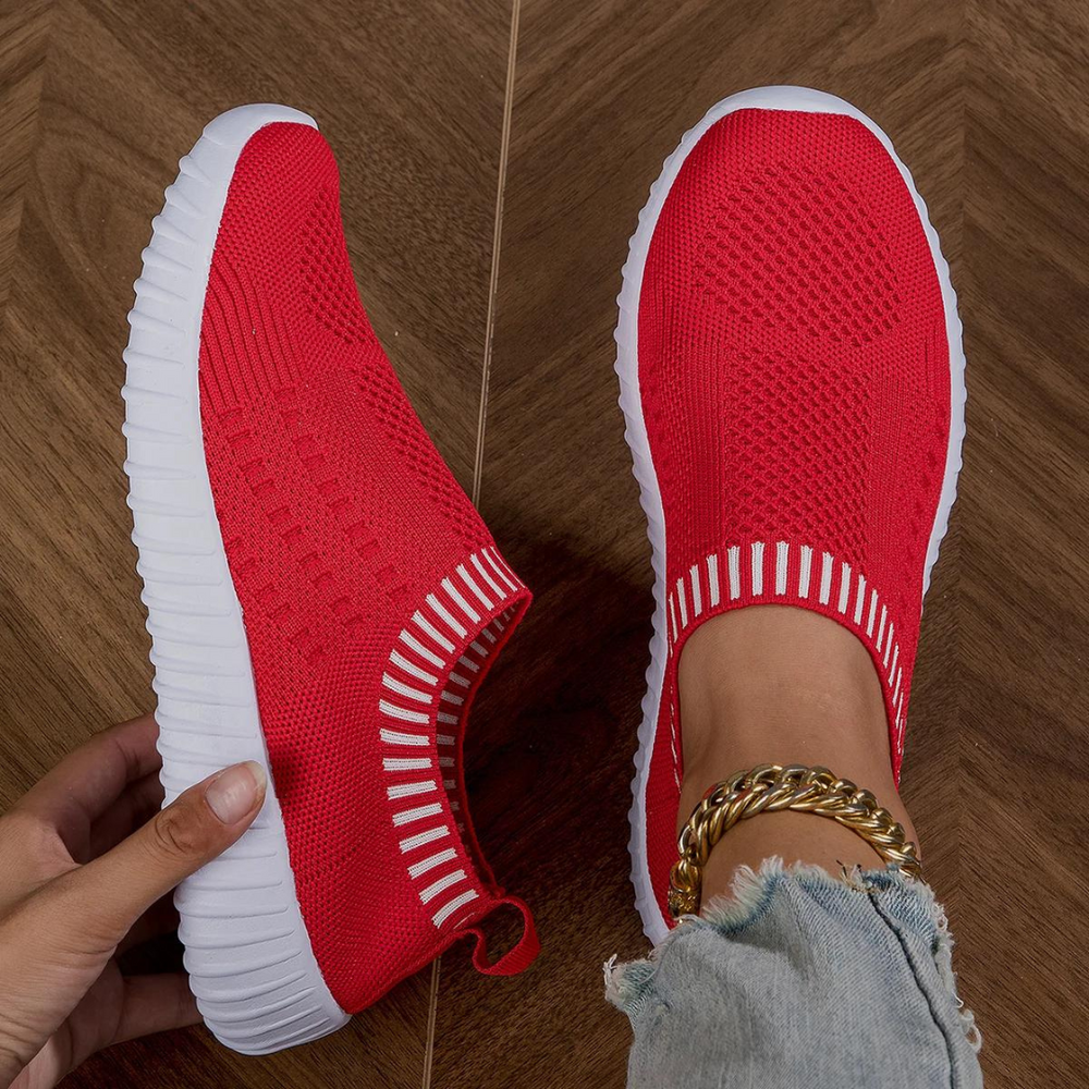 Rote Damen-Sneaker mit weißer Sohle, gestricktes Obermaterial, getragen auf Holzfußboden. Modische, bequeme Schuhe für Freizeit und Sport.