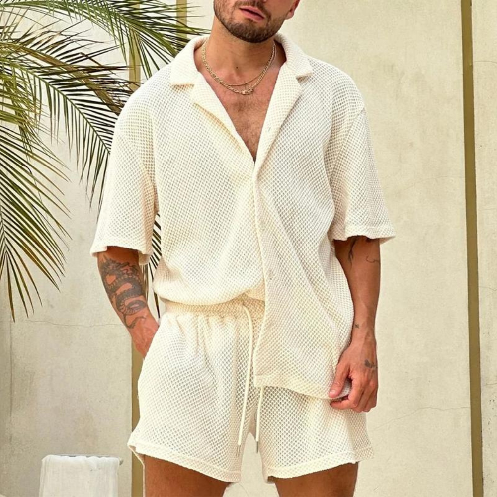 Ein Mann trägt ein cremefarbenes, strukturiertes Sommer-Set aus Hemd und Shorts. Lässige Herrenmode, ideal für warme Tage.