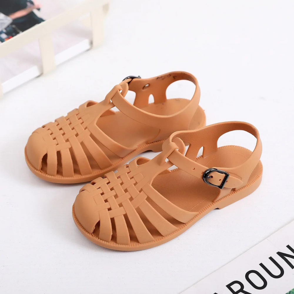 Braune Sandalen aus Kunststoff mit geflochtenem Design und verstellbarem Riemen auf weißem Hintergrund. Ideal für Sommermode und Strandkleidung.