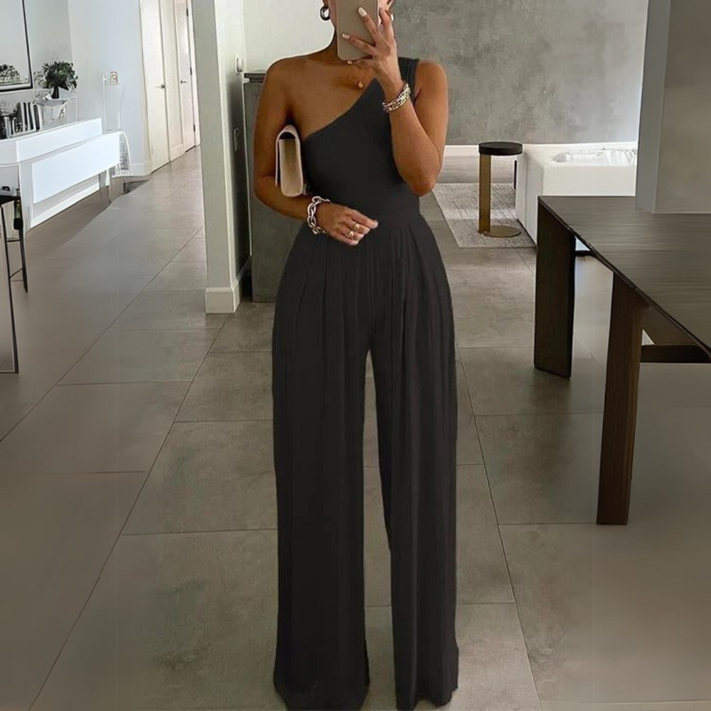 Frau in elegantem, schwarzem, schulterfreiem Jumpsuit in modernem Wohnzimmer. Stilvolle Abendmode, modisches Design, zeitloser Chic.