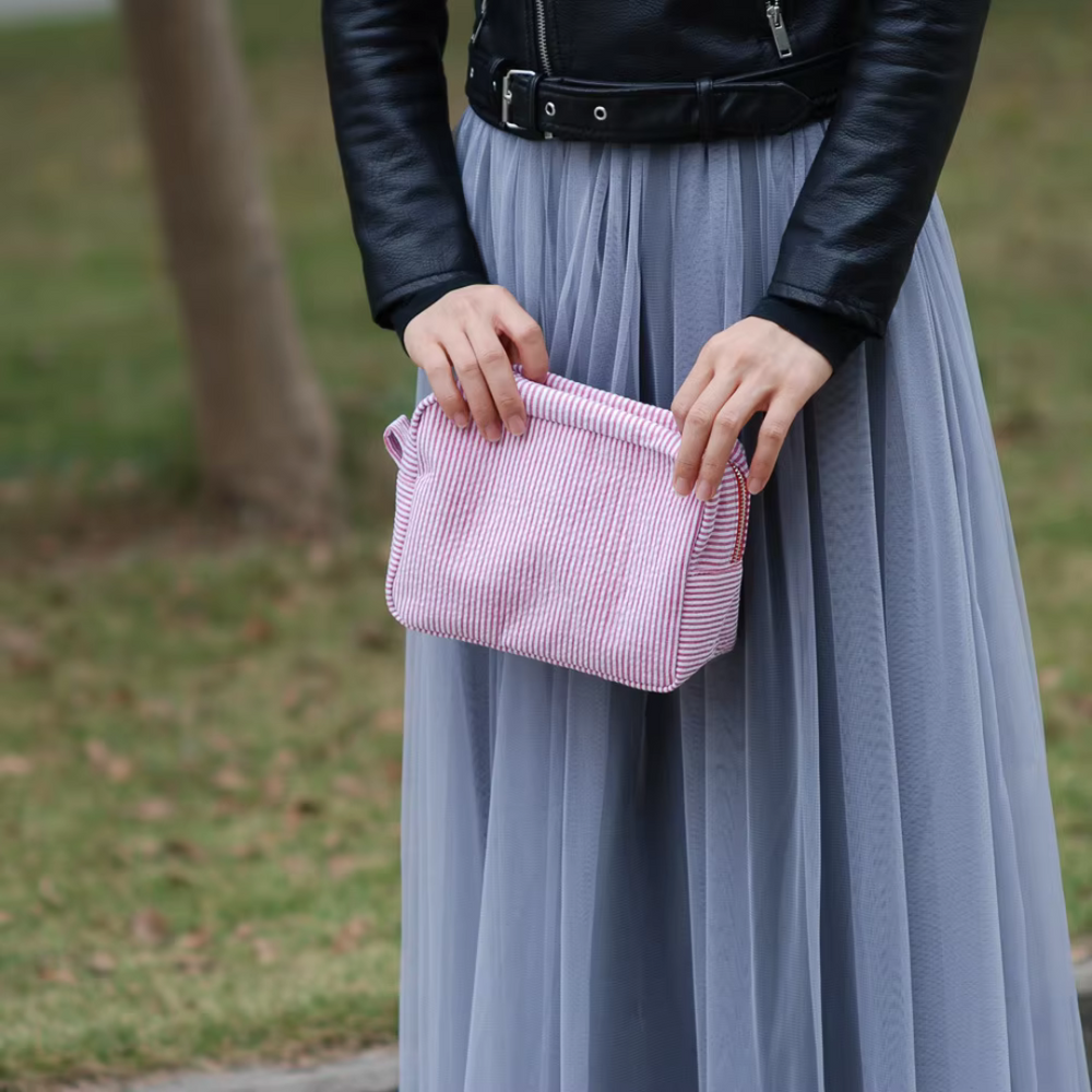Frau in schwarzer Lederjacke und grauem Tüllrock hält eine rosa gestreifte Handtasche. Mode, Streetstyle, Damenbekleidung, Accessoires.