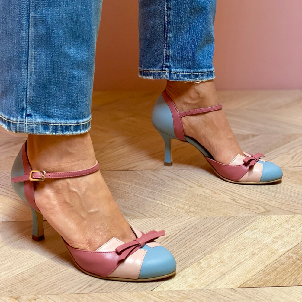 Frau trägt elegante, mehrfarbige Pumps mit Schleifen, kombiniert mit blauen Jeans. Modische Damenschuhe, stilvoller Look, Holzboden.