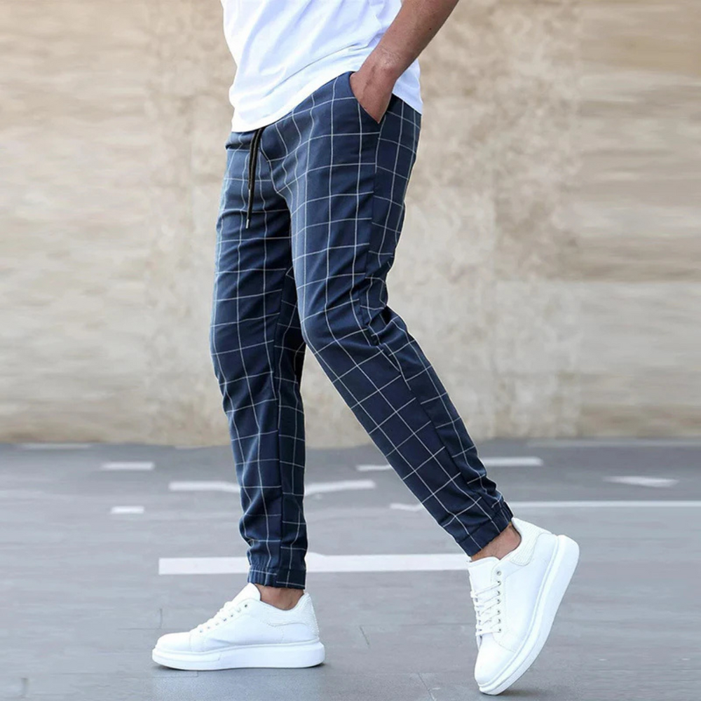 Mann in karierten Jogginghosen und weißen Sneakers, seitlich gehend. Modetrend, Freizeitlook, Herrenbekleidung, stilvolle Jogginghose.
