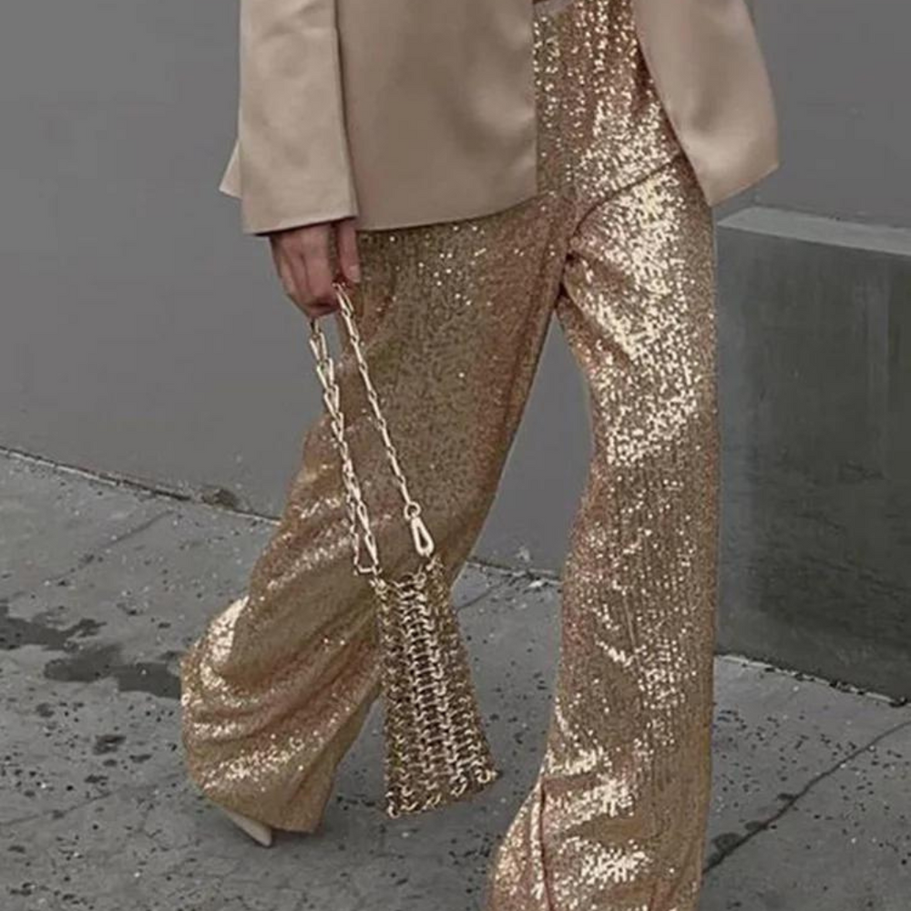 Elegante goldene Paillettenhose und passende Tasche, getragen von Person in beigem Blazer. Glänzende Mode, glamouröser Look, Streetstyle.