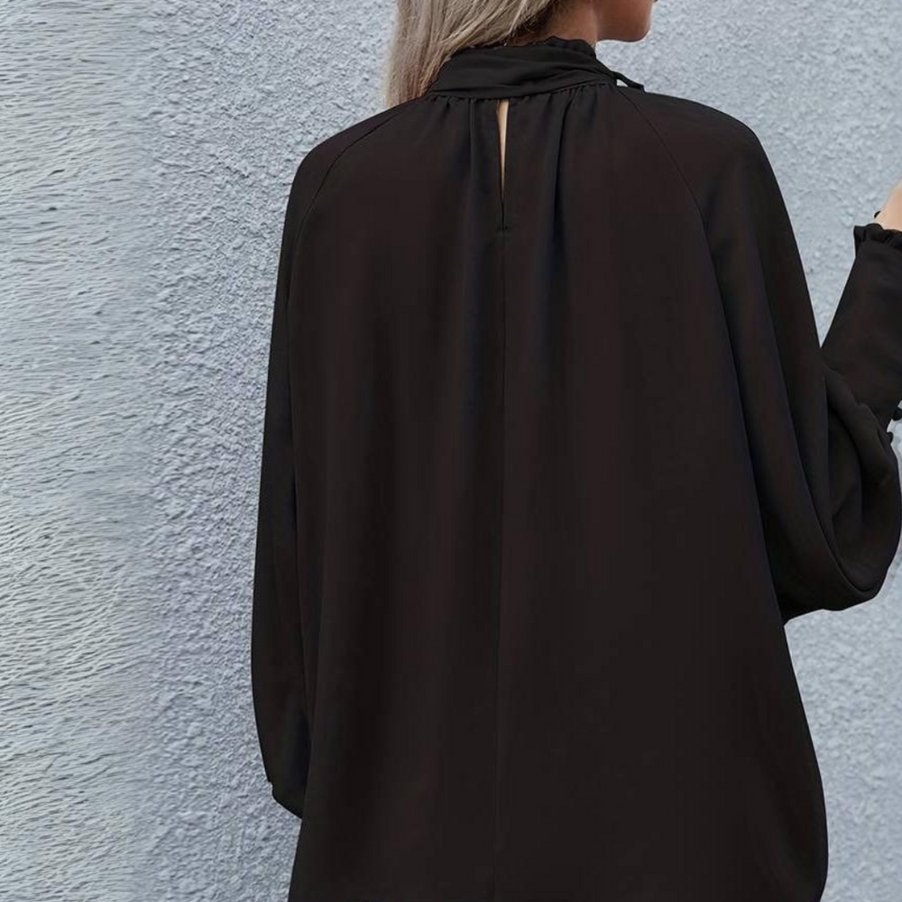 Frau in schwarzer Bluse mit langen Ärmeln vor grauer Wand, modisches Damenoberteil, elegantes Design, Herbstmode 2023.