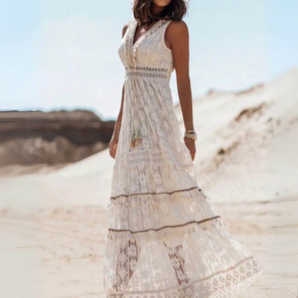 Frau in weißem Spitzenkleid steht in Wüste, Boho-Stil, Sommermode, ärmelloses Maxikleid, elegantes Design, natürliche Umgebung, modisches Outfit.