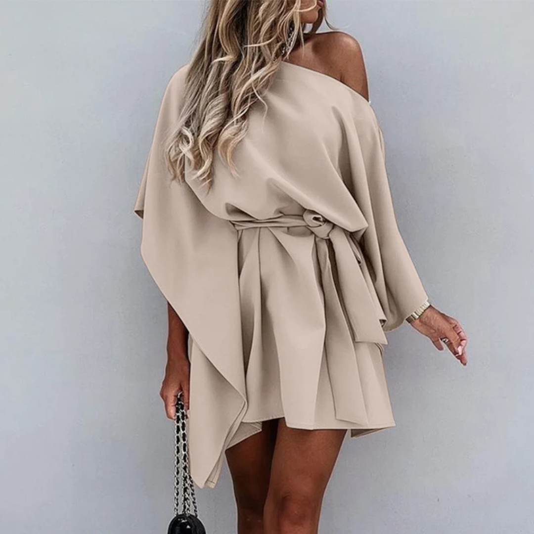 Frau in elegantem, beigem, schulterfreiem Kleid mit Gürtel, welliges Haar, hält schwarze Handtasche. Modetrend, Damenmode, schickes Outfit.