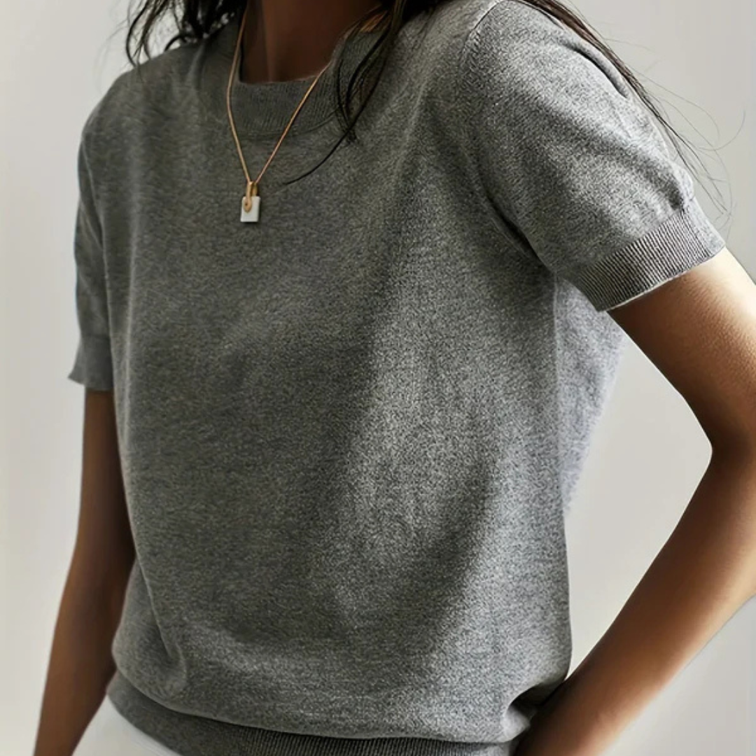 Frau in grauem T-Shirt mit kurzen Ärmeln und goldener Halskette. Modetrend, lässiger Stil, minimalistisch, elegantes Design.