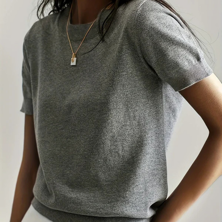 Frau in grauem T-Shirt mit kurzen Ärmeln und goldener Halskette. Modetrend, lässiger Stil, minimalistisch, elegantes Design.