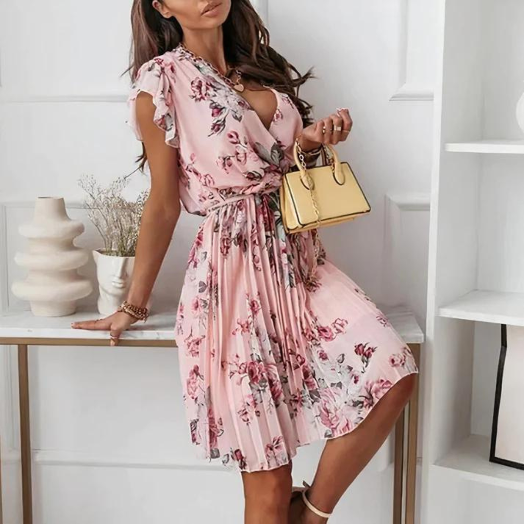 Frau in rosa geblümtem Kleid mit V-Ausschnitt, hält eine kleine gelbe Handtasche. Elegante Sommermode, femininer Stil, modisches Outfit.