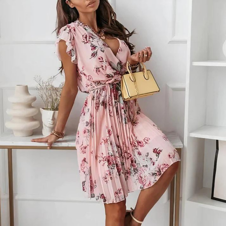 Frau in rosa geblümtem Kleid mit V-Ausschnitt, hält eine kleine gelbe Handtasche. Elegante Sommermode, femininer Stil, modisches Outfit.