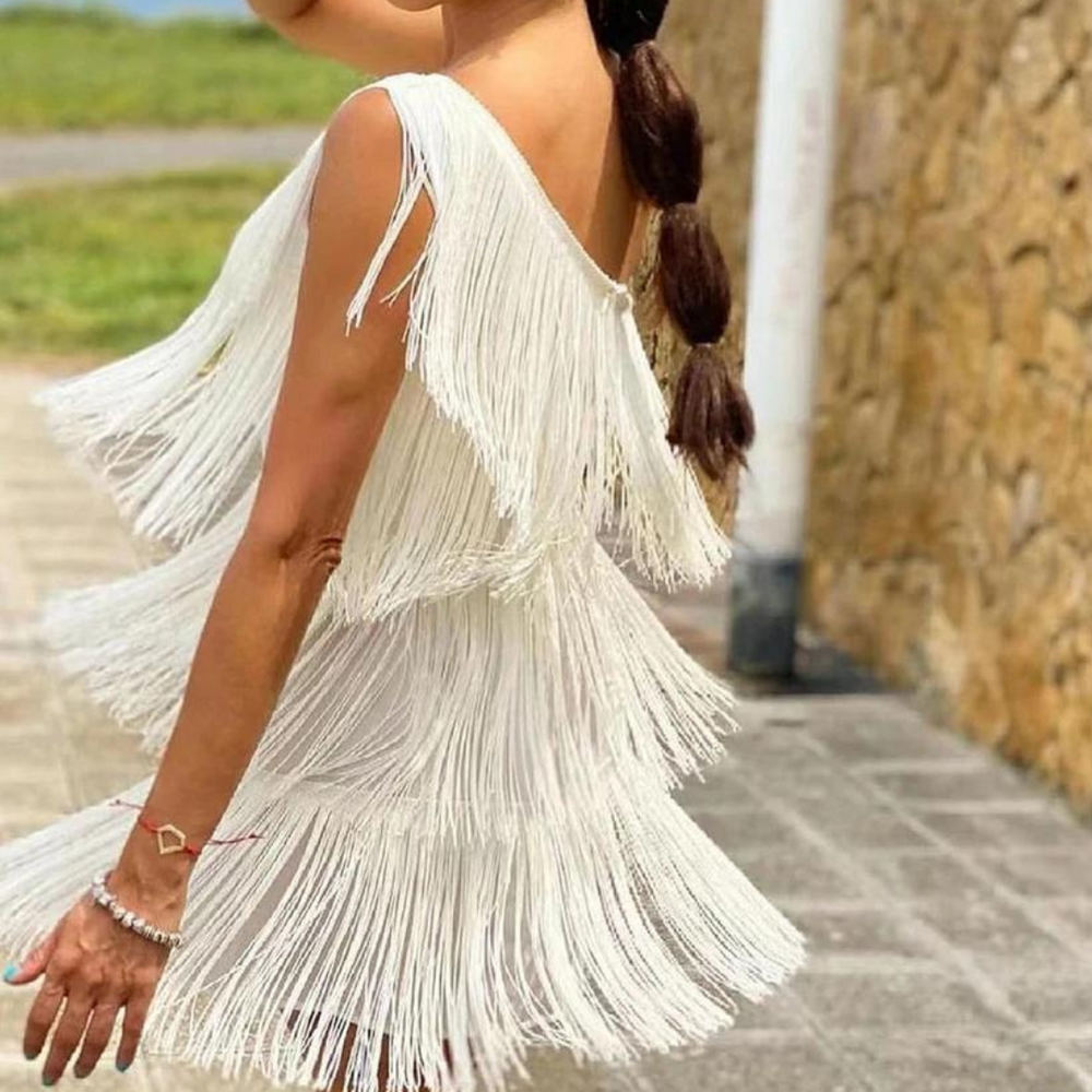 Frau in weißem Fransen-Kleid, seitlich fotografiert, mit geflochtenem Zopf. Sommermode, elegantes Design, Outdoor-Hintergrund.