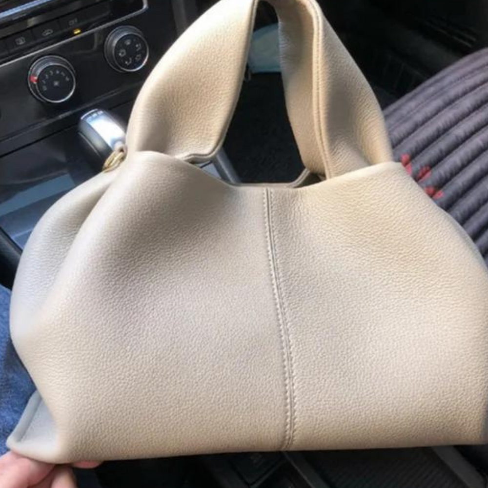 Beigefarbene Lederhandtasche im Auto, modernes Design, weiches Material, luxuriöses Accessoire, ideal für stilvolle Damenmode.