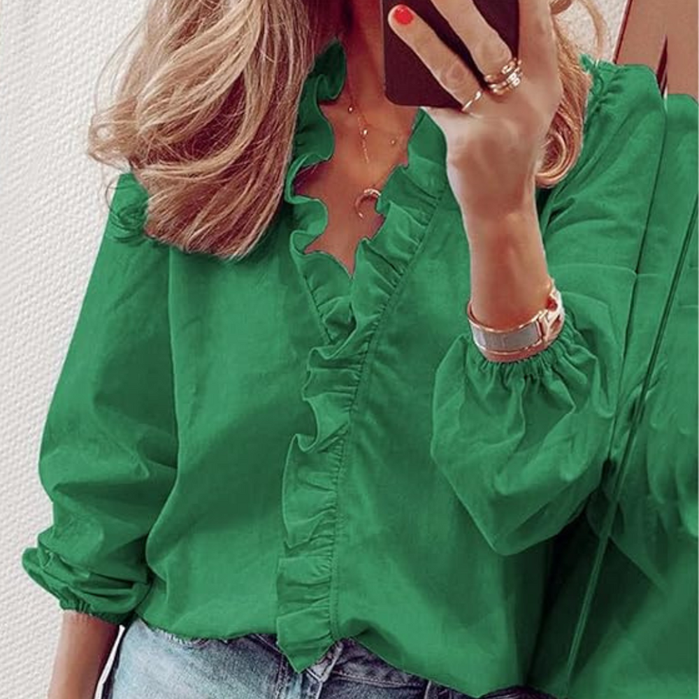 Frau mit grüner Rüschenbluse und blonden Haaren, hält Smartphone. Modetrend, Damenmode, stilvolle Kleidung, Freizeitlook.