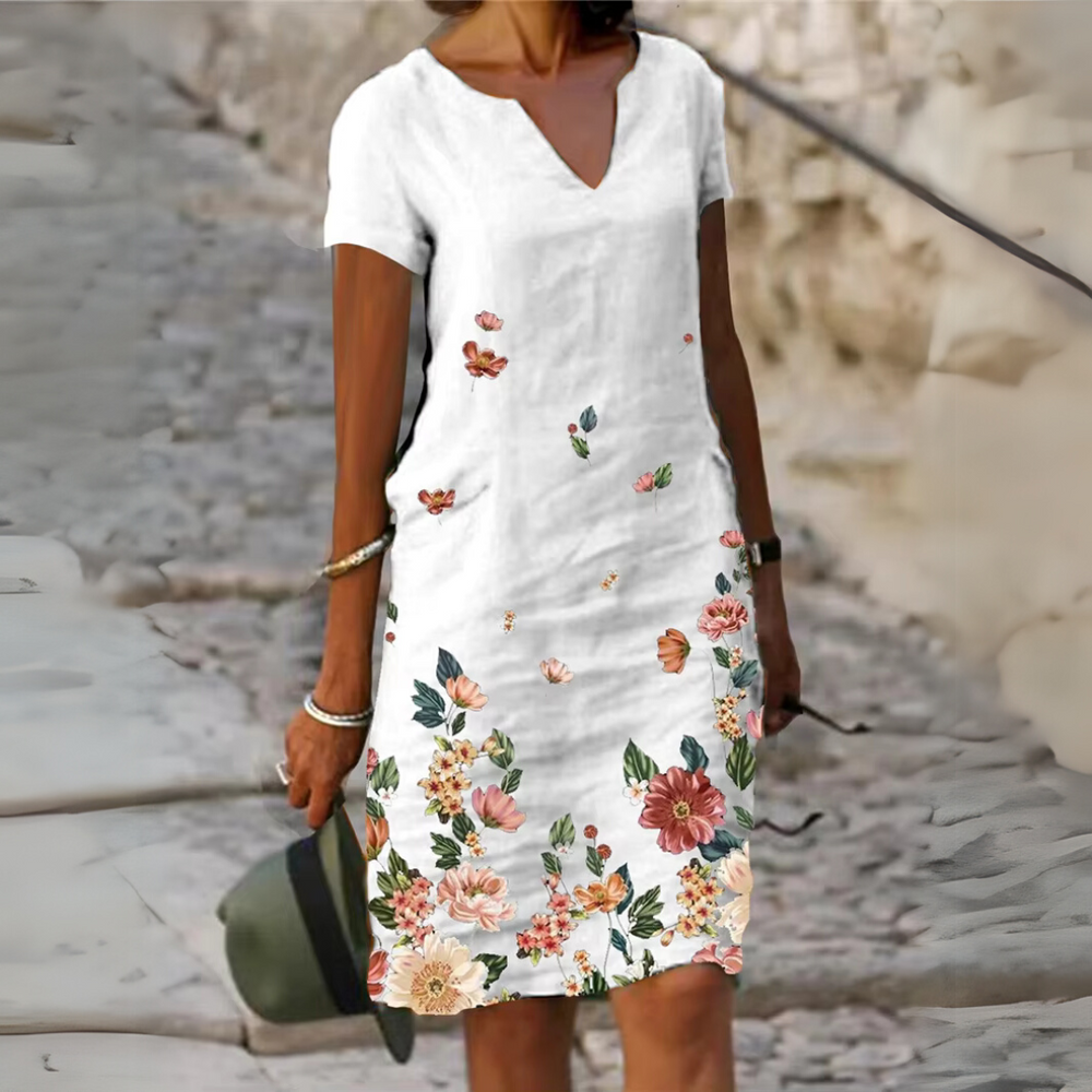 Frau in weißem Sommerkleid mit Blumenmuster, steht auf gepflastertem Weg. Elegantes Design, modische Sommermode, Freizeitkleidung für Damen.