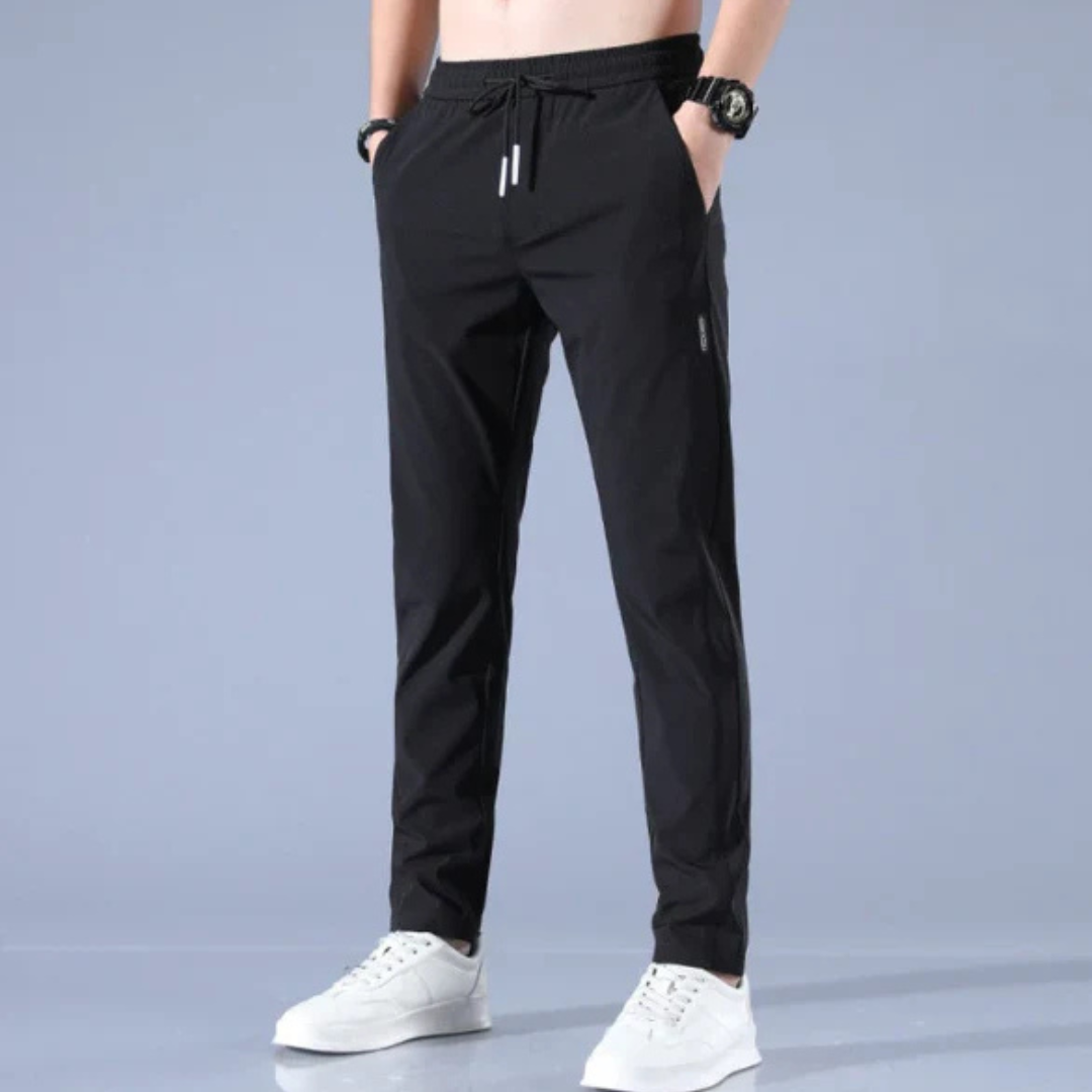 Mann in schwarzen Jogginghosen und weißen Sneakers vor grauem Hintergrund. Sportliche Kleidung, Freizeitmode, Herrenbekleidung.