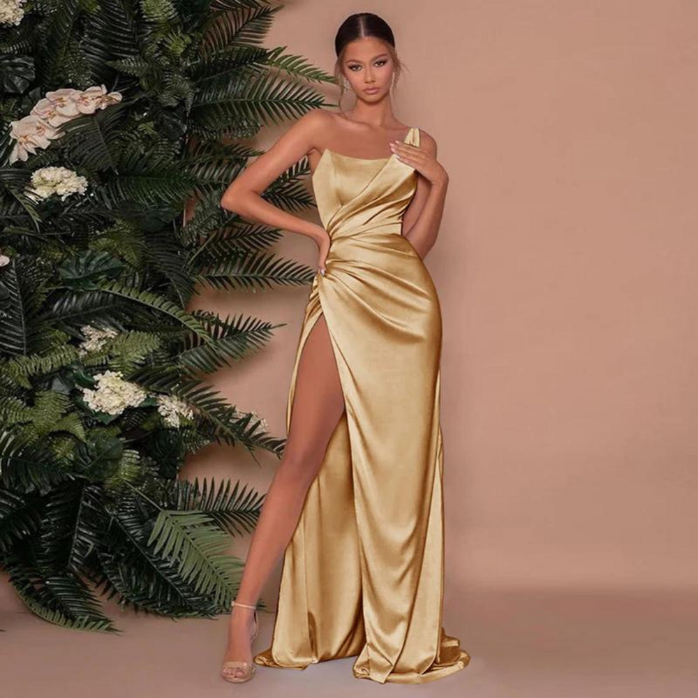 Elegantes Abendkleid in Gold mit hohem Beinschlitz, getragen von einer Frau vor einem Hintergrund aus grünen Pflanzen. Perfekt für formelle Anlässe.