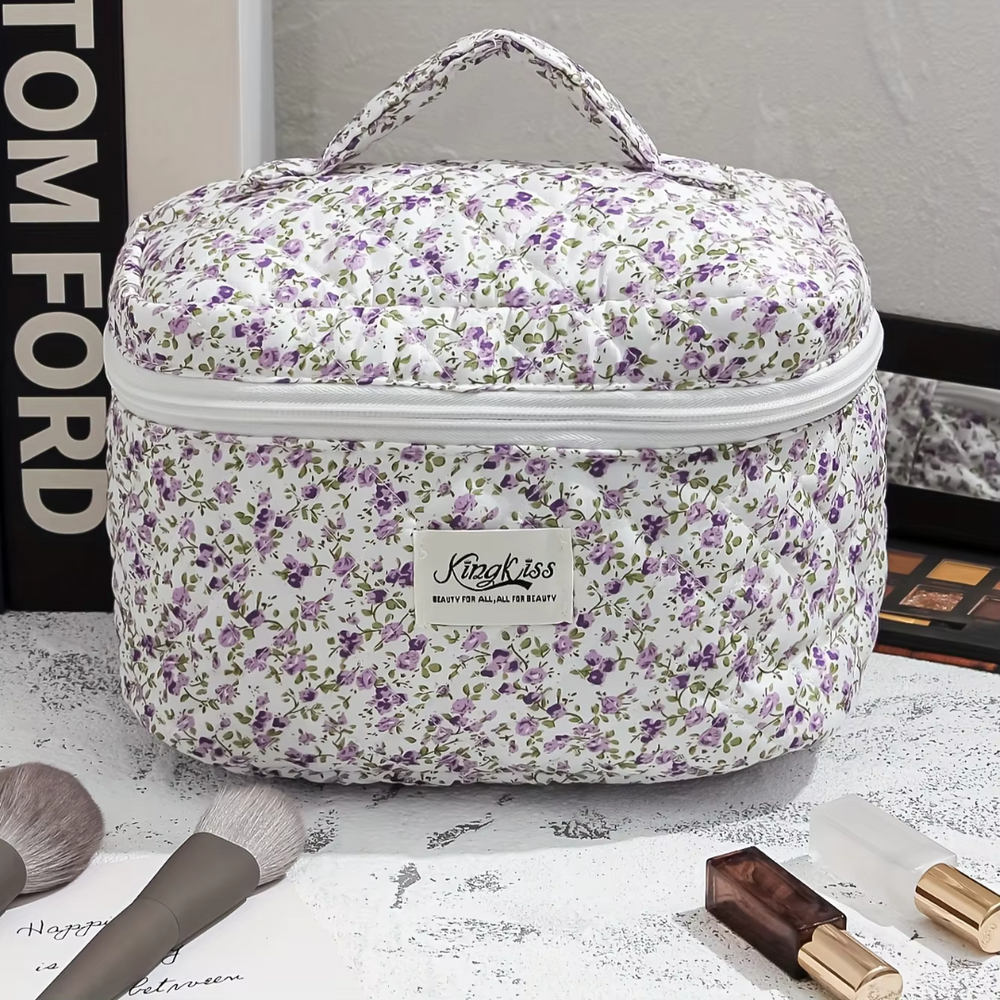 Kosmetiktasche mit lila Blumenmuster, Reißverschluss und Tragegriff, auf Schminktisch mit Make-up-Pinseln und Lippenstift. Ideal für Reisen.