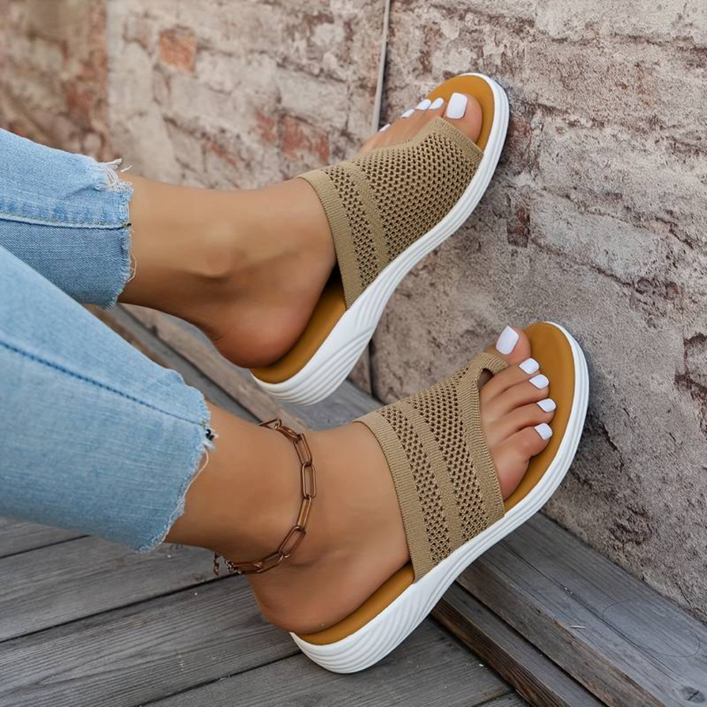 Damenfüße in beigen Sandalen mit Keilabsatz und Strickmuster, kombiniert mit hellblauen Jeans. Perfekte Sommermode für Damen.