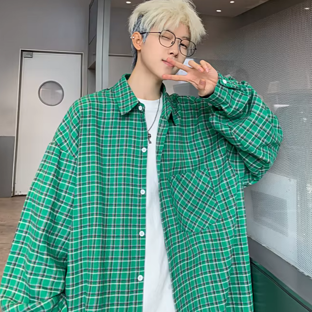 Junger Mann mit blonder Frisur und Brille trägt ein grünes kariertes Hemd und zeigt ein Peace-Zeichen. Moderner Streetwear-Look, urbaner Stil.
